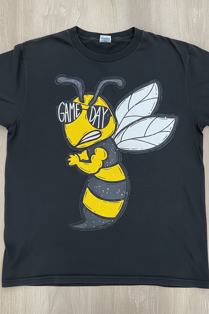 T-shirt arranged on a wood floor. The shirt features yellow and black graphics related to 'Jackets Game Day' and a bee design