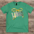 green heathered t-shirt featuring a graphic that spells 'Lions' with a large ribbon bow above it. The letters are filled with various patterns including stripes, checkers, and chevrons in yellow, white, black, and green.